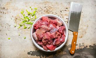Chopped raw meat in a bowl with green onion and a knife for cutting meat. photo