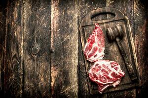 Raw meat background. Steaks of raw meat with a hammer on the old Board. On wooden background. photo