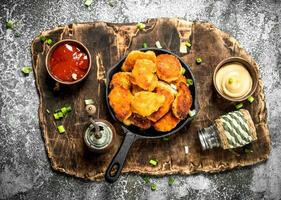 Chicken nuggets in a pan with different sauces. photo