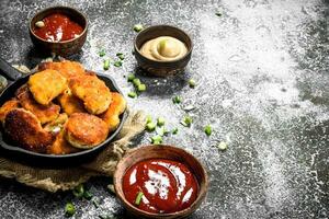 Chicken nuggets in a pan with different sauces. photo