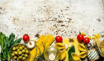 Pasta background. A lot of different pasta, olives, tomatoes, oil and herbs. photo