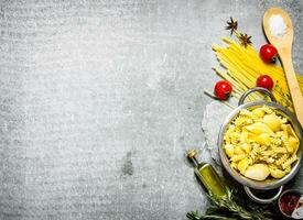 Boiled pasta in the pan with olive oil and tomatoes. photo