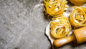 Dry pasta with a rolling pin and flour. photo