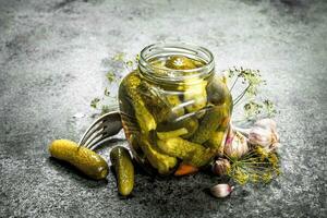 Marinated cucumbers with garlic, spices and herbs in glass jar. photo