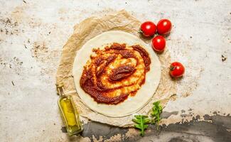 The rolled out pizza dough with tomato paste, olive oil and tomatoes. photo