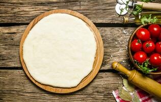 Pizza dough with tomatoes, and herbs with a rolling pin. photo