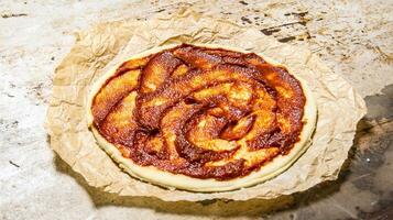 The rolled out pizza dough with tomato paste on old paper. photo