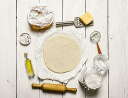 Roll out the pizza dough and ingredients - flour, cheese, olivkovoe oil. photo