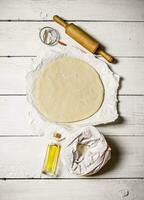 Pizza dough with a rolling pin. On white wooden background. photo