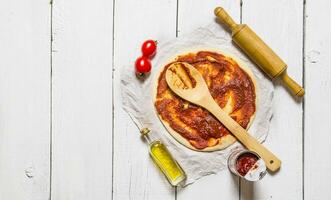 The rolled out pizza dough with tomato sauce and with a rolling pin. photo