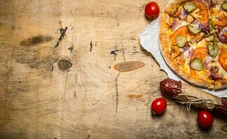 Pizza with bacon and salami on paper. On wooden table. photo