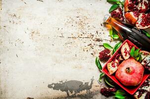 Pomegranate juice in a bottle and pieces of pomegranate with leaves. photo