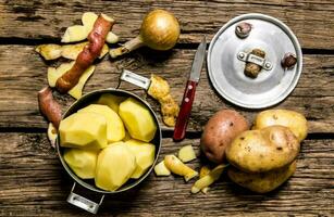 Peeled potatoes in an old pan with knife on wooden table . photo