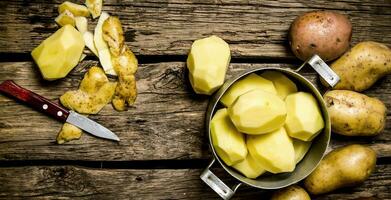 Peeled potatoes in an old pan with knife on wooden table . photo