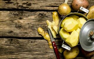 Peeled potatoes in an old pan with knife on wooden table . Free space for text. photo