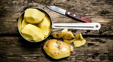 Peeled potatoes in an old pan with knife on wooden table . photo
