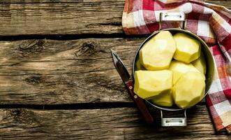 Peeled potatoes in an old pan with knife on wooden table . Free space for text. photo