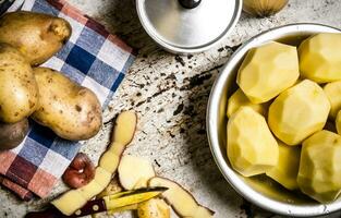 The peeled potatoes in a metal bowl on the rustic background . photo