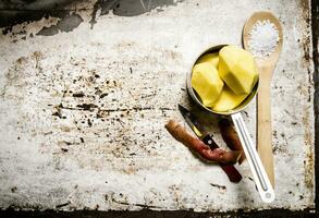 The peeled potatoes in a metal saucepan with a spoonful of salt on the rustic background . Free space for text. photo