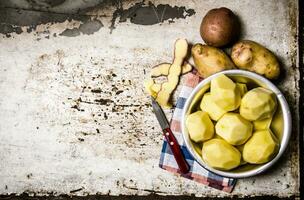 The peeled potatoes in a metal bowl on the rustic background . Free space for text. photo