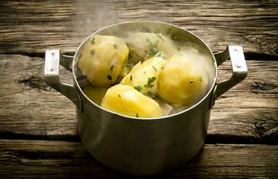 Boiled potatoes with herbs and steam on a wooden table . photo