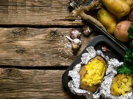 Baked potatoes in foil with salt and garlic on a wooden table . Free space for text. photo