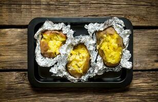 Baked potatoes in foil on a wooden table . photo