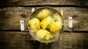 Boiled potatoes with herbs and steam on a wooden table . photo