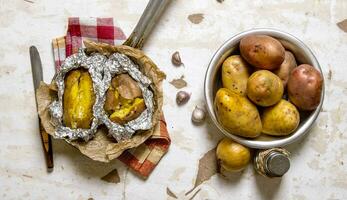 The concept of baked potato in foil on an old rustic table . photo