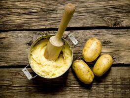 Cooking mashed potatoes with pestle on wooden background. photo