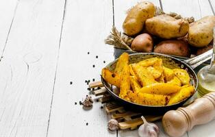 The concept of baked potatoes in a skillet with spices on a white wooden table. Free space for text. photo