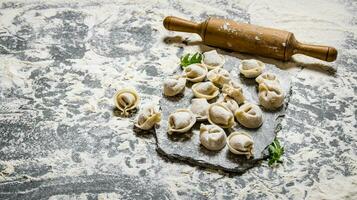 Home-made ravioli with a rolling pin on a stone stand. On stone table with flour. photo