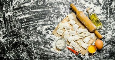 Raw homemade ravioli with egg, flour and a rolling pin. photo