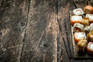 Japanese food. Fresh rolls seafood with a chopstick. On the old wooden background. photo