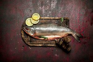 Whole fish on a cutting Board with lemon and spices. On rustic background. photo