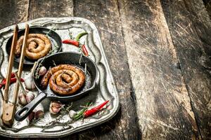 Sausages in pans on a steel tray with hot chili peppers. photo