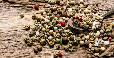 Spicy peppercorns in a spoon. On wooden background. photo