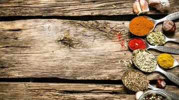 Different kinds of spices in spoons. On wooden background. photo