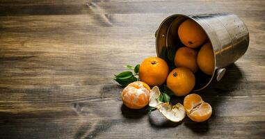 Fallen bucket with fresh tangerines. On wooden table. photo