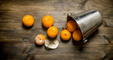 Fallen bucket with fresh tangerines. On wooden table. photo