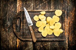 The sliced potatoes on an old wooden Board. On wooden background. photo