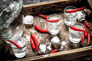 Vodka shots with chili peppers on a wooden tray. photo