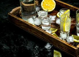 Vodka with lemon and ice on a wooden tray. photo