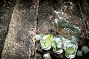 Vodka shots with lime and ice on the board. photo