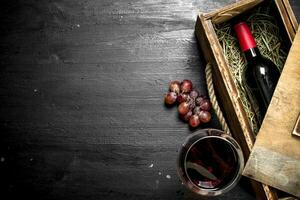 botella de rojo vino en un antiguo caja con un rama de uvas. foto