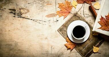 taza de café con un antiguo libro y arce hojas. foto