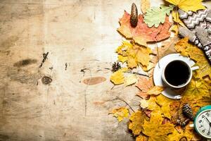 Cup of coffee with alarm clock on autumn leaves. photo