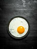 Fried egg in a frying pan. On black wooden background. photo