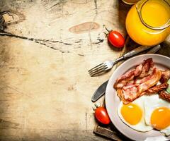 Orange juice with fried eggs, bacon, and slices of bread. photo