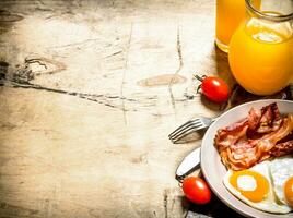 Orange juice with fried eggs, bacon, and slices of bread. photo